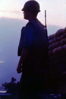 An American soldier standing near a sandbag wall at either dusk or dawn.