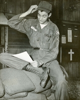 "Saigon - While the offer sounds tempting, PFC Ronald A. Roach (1967 Portola Way, Stockton, Calif.) doubts that Army authorities in Vietnam will allow him to go home to accept a call from his local draft board. Roach, serving with the U.S. Army's 1st Logistical Command at Tan Son Nhut, enlisted in the Regular Army last January." An American soldier reads a piece of paper and sits on  a sandbag wall.