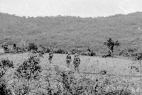 Three American soldiers walking through a field up a slight hill