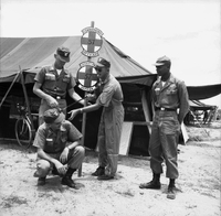 Four American soldiers pose next to sign - one has a small monkey on his shoulder and the other is trying to control it with a leash.