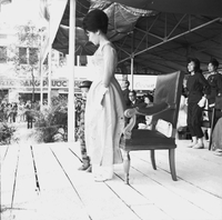 Original caption: "Mne. Nhu + Paramilit. Graduation - 27 Feb 63" Madame Nhu (Tran Le Xuan) standing in front of her chair on a stage.