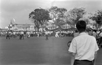 "Unidentified", Photo of a protest. A large crowd of Vietnamese people walk in a major intersection with banners. Men riding bikes and motorcycles have stopped to watch in the foreground.