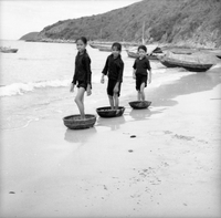 Three young Vietnamese girls are standing in baskets on a shoreline.