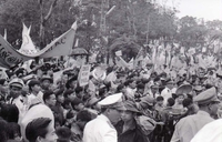 A crowd of Vietnamese people holding flags and banners. They have both American and South Vietnamese flags.