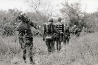 Several American soldiers walking through a field in a line.