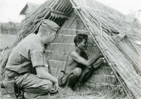 An American soldier named Hibbs watches as a villager attaches something to his thatched house.