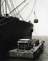 "Loading Up - LCM-8 #870 takes cargo aboard starboard-side to S.S. Sir John Franklin as Hatch Team #9 offloads combat tents destined for the Marines. "870" is one of the LCM-8's which deliver the cargo from ship to shore." Cargo is unloaded from a large Navy ocean liner onto a small barge.