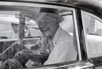 Henry Cabot Lodge Jr wearing a hat is seated inside of a vehicle. He smiles at the camera.