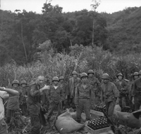 A group of ARVN soldiers surround some supplies in a field.