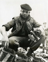 "Lieutenant (junior grade) James F. Morgan, Jr., USN, of Havertown, Pa., examines an enemy sighting device recovered from sampan in which at least 15 enemy soldiers were killed by U.S. Navy Forces early today. The action occurred as the sampan attempted to cross the Mo Nhat River in Phuoc Tuy Province, 27 miles southeast of Saigon. Carrying case for the Russian-made weapon sight is at lower left." An American sailor holds a piece of sighting equipment.  More equipment sits in front of him, including some metal equipment cases. Another American sailor is in the background in the right of the frame.