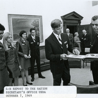 Original caption: "4-H report to the Nation Secretary's Office USDA October 7, 1969." Clifford Hardin looks at a scrapbook with a representative of 4-H, with four additional unidentified representatives looking on, an unidentified woman and two unidentified men stand in the office doorway.